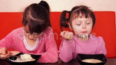 孩子们吃<strong>粥</strong>。 两个小女孩吃<strong>粥</strong>。 两个姐妹坐在橙色的沙发上吃晚饭。